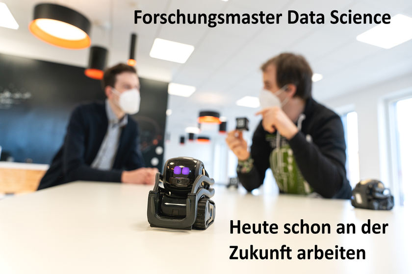 Titelbild des Forschungsmasters. 2 Studierende diskutieren im Hintergrund. Im Vordergrund ist ein kleiner Roboter zu sehen.