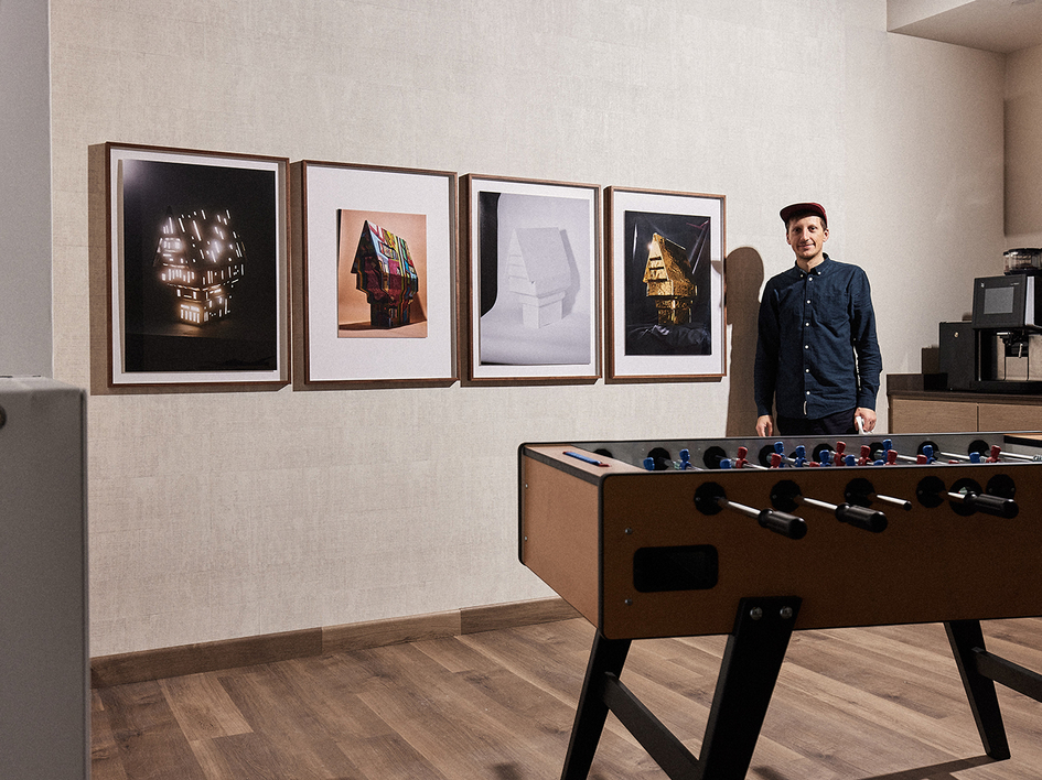 Patrick Pollmeier im Hotelraum neben seinen vier Fotografien von Modellhäusern an der Wand