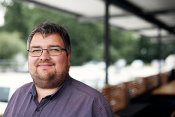 Porträbild von Matthias Pieper der in einem weinroten Hemd vor der Fertigungshalle des Unternehmens fast52 steht Er trägt eine Brille und hat kurzes braunes Haar