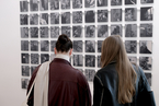 Zwei Frauen stehen vor einer Serien von Fotos, die zu einem Quadrat angeordnet sind