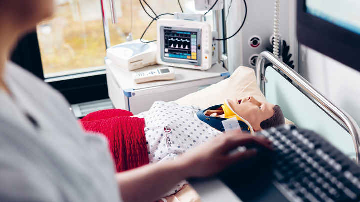 Studierende im Vordergrund gibt Daten ein im Hintergrund ist eine Puppe im Krankenbett