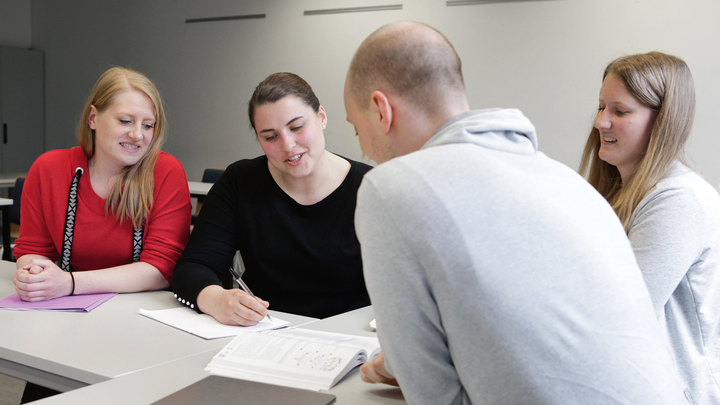 Eine Gruppe Studierender sitzen am Tisch und diskutieren.